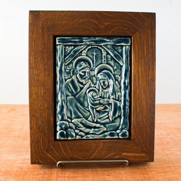 The Nativity Tile features the haloed holy family - Joseph, Mary and Baby Jesus - embracing under the wooden beams of the stable. Behind them, a window in the stone wall gives a glimpse of the Bethlehem star. This tile is in our glossy deep blue Ocean glaze which beautifully offsets the yellowish brown oak wood frame.