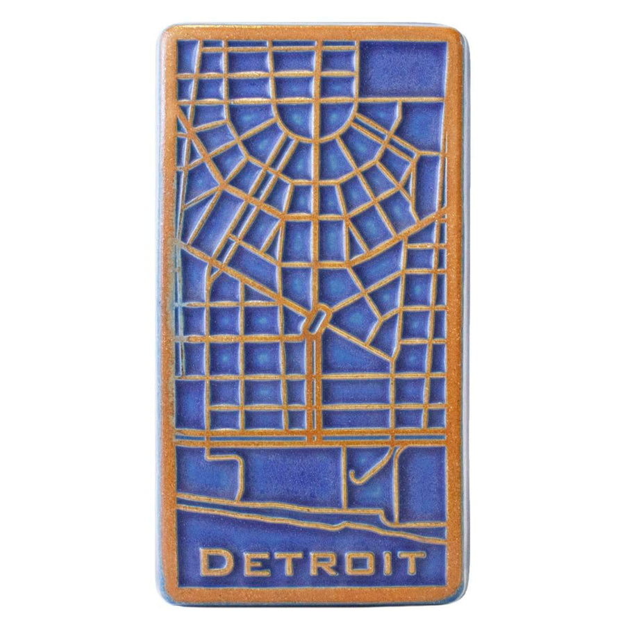 The raised areas of this tile - the word Detroit and the street lines - are scraped which means that it has an orange color while the background is a dark matte blue glaze.