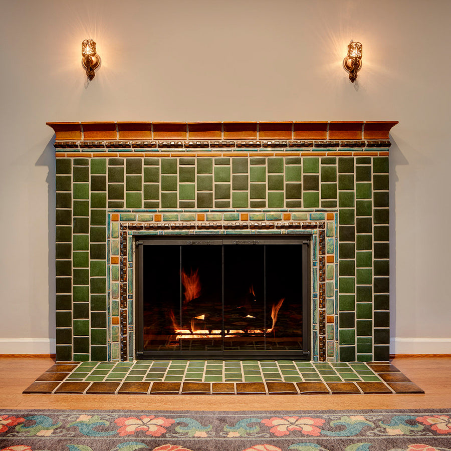 Warm chestnut glazed tiles make up the trim of this fireplace with bayleaf and assorted green glazed tiles at the center. 