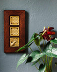 This framed triptych features one Honey Bee Tile and two Honeycomb tiles. The Honeybee Tile features a large honeybee with stripes and detailed segmented wings sitting on a honeycomb patterned background. The Honeycomb tiles are a flat line drawing of a honeycomb pattern with a simple smooth border around it. These three tiles are lined up and attached in a deep reddish brown oak frame.