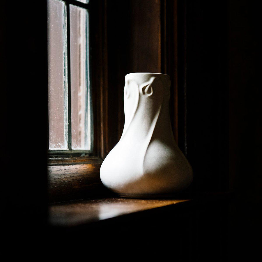 A Snowdrop vase sits on a windowsill, the light trickling in seems to warm the ceramic.