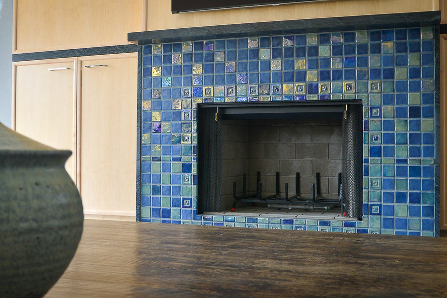 A blue iridescent tiled fireplace with accent tile around the center and custom-cut tile radiating from the center of the design. 