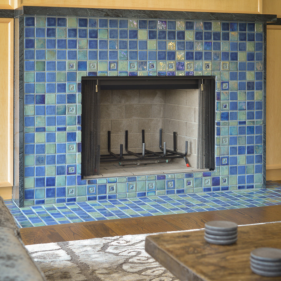 A close up shot of a blue iridescent tiled fireplace. The details in the accent tiles are more visible surrounding the fireplace's opening. 