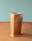 The pale brown tumbler boasts a semi-gloss glaze and a slight triangle shape.