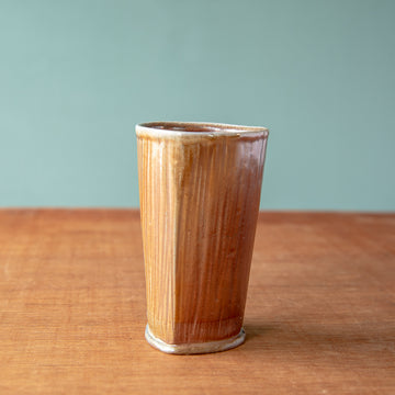 The pale brown tumbler boasts a semi-gloss glaze and a slight triangle shape.