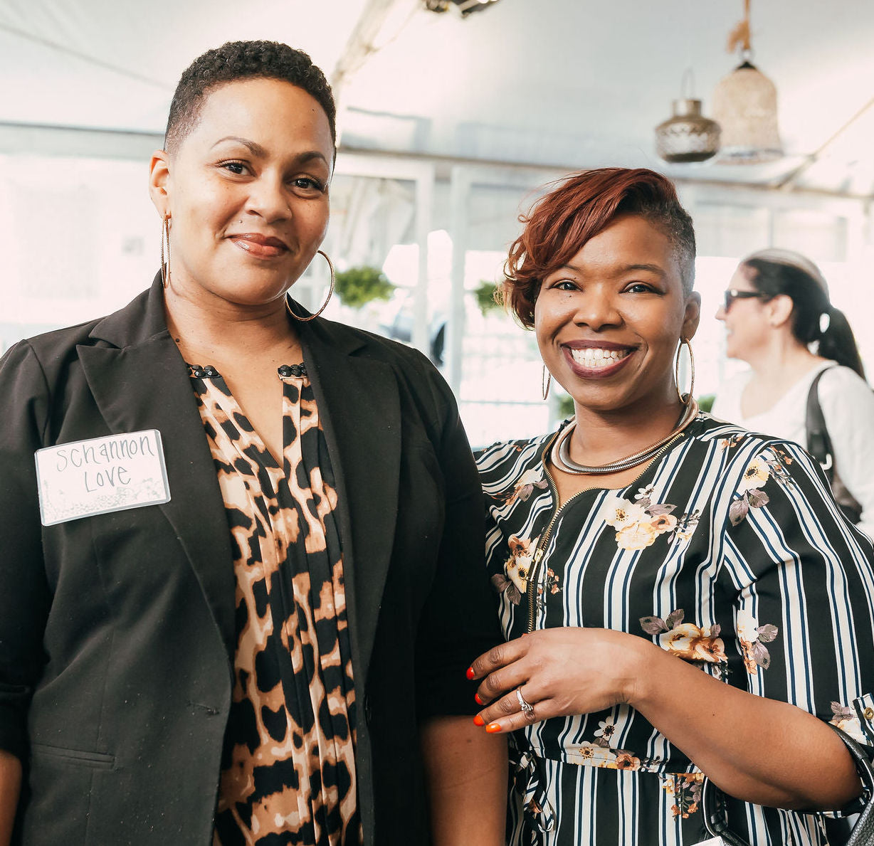 Two ladies smile and pose for a photo with black white and tan patterned attire