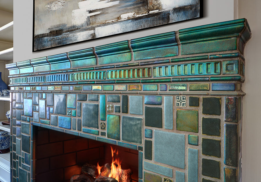 Vibrant, lit fireplace made up of Iridescent and matte glazes which creates an overall green, mirror-like effect. This detailed shot shows the complexity of the custom-cut accent trim tiles.