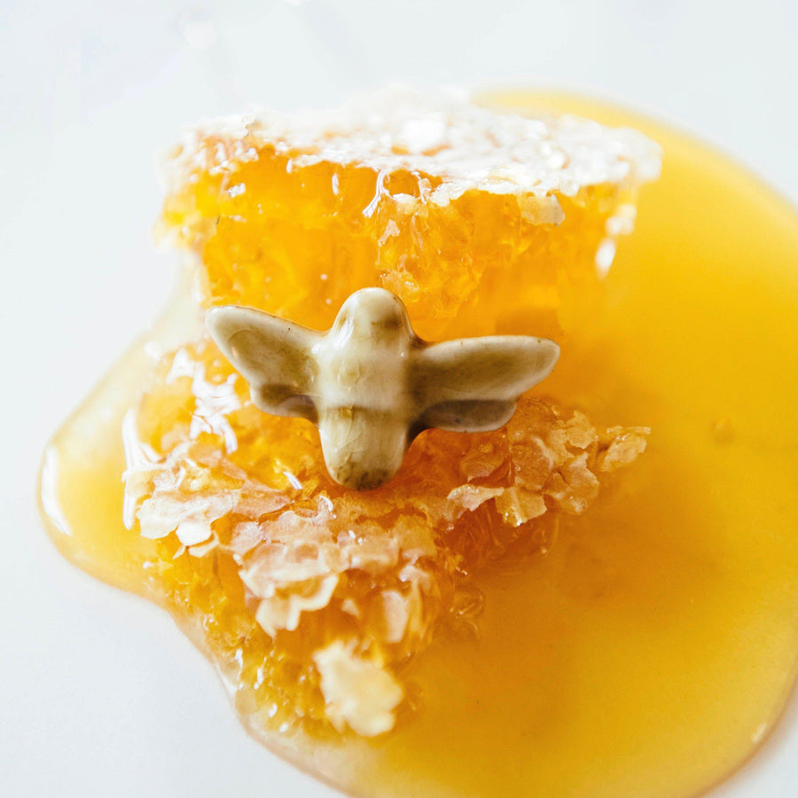 The Honey Gloss glazed bee pin is resting on a bed of sticky honey.