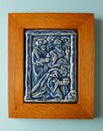 The Three Wise Men Tile features the wisemen in robes holding their three gifts- gold, frankincense and myrrh. They are all facing the right, they seem to be focused on one point. There is a stone wall behind them. This tile is in the glossy deep blue Ocean glaze which offsets the pale yellowish brown oak wood frame.