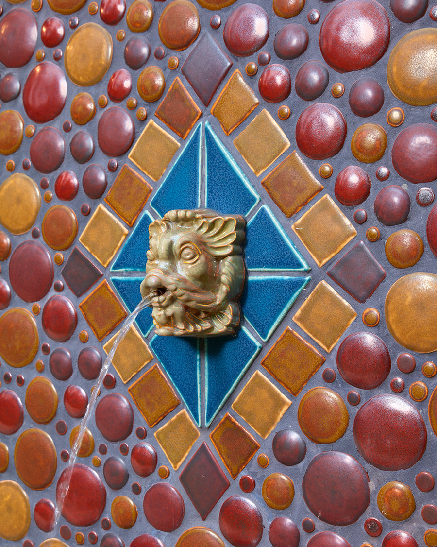 In the center of the installation is the golden face of a stylized fish. Its lips are pursed and water is shooting out of its mouth.