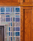 A detail shot of a fireplace and hearth made up of blue, gray, and charcoal tiles. The camera is focused on a corner of the fireplace, which shows the wood grain detail of the Craftsman style mantel surround.