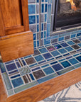 A detail shot of a fireplace and hearth made up of blue, gray, and charcoal tiles. 