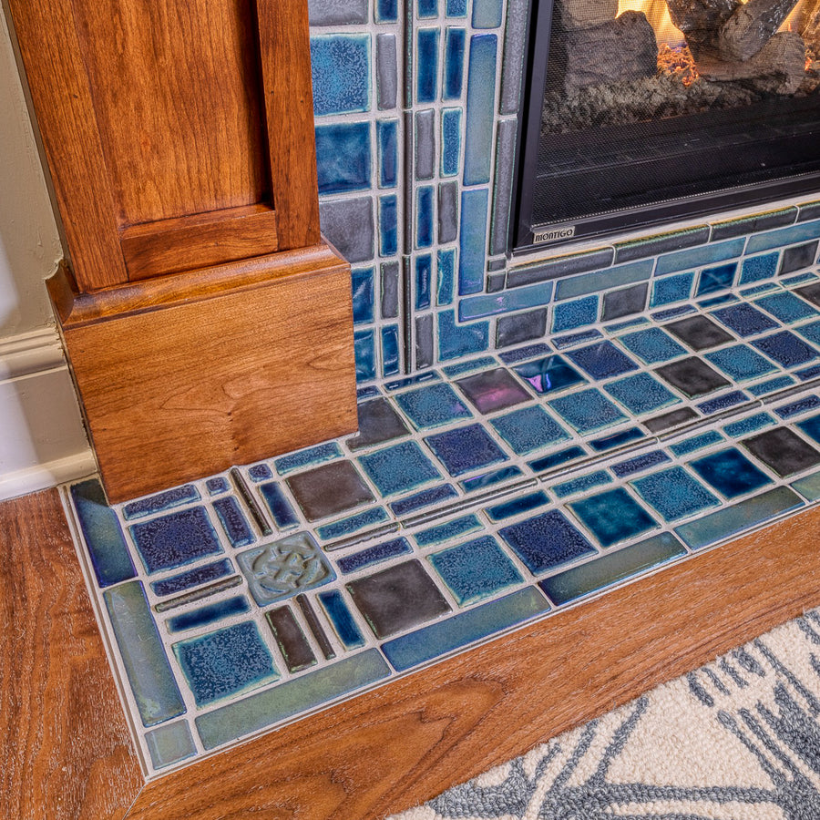 A detail shot of a fireplace and hearth made up of blue, gray, and charcoal tiles. 