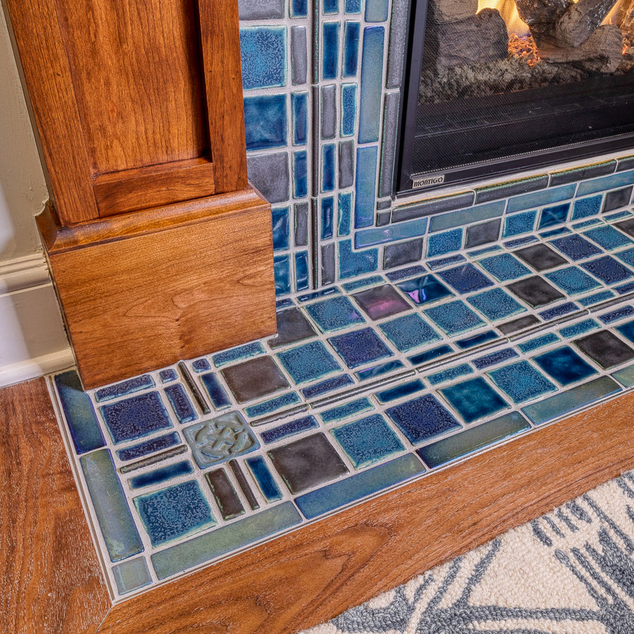 A detail shot of a fireplace and hearth made up of blue, gray, and charcoal tiles. 