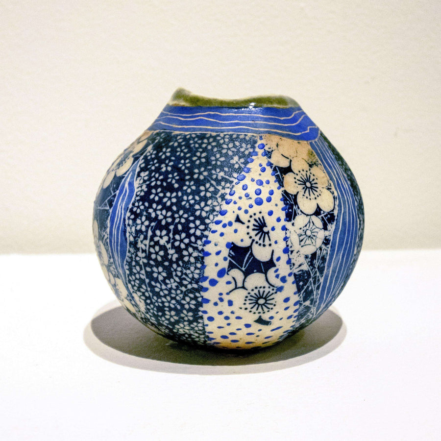 This small, irregular round vase has strips of blue and white floral patterns - some small and some large - that look almost stitched together.