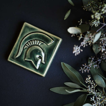 A Kale colored tile rests on a table with seeded eucalyptus bordering it.