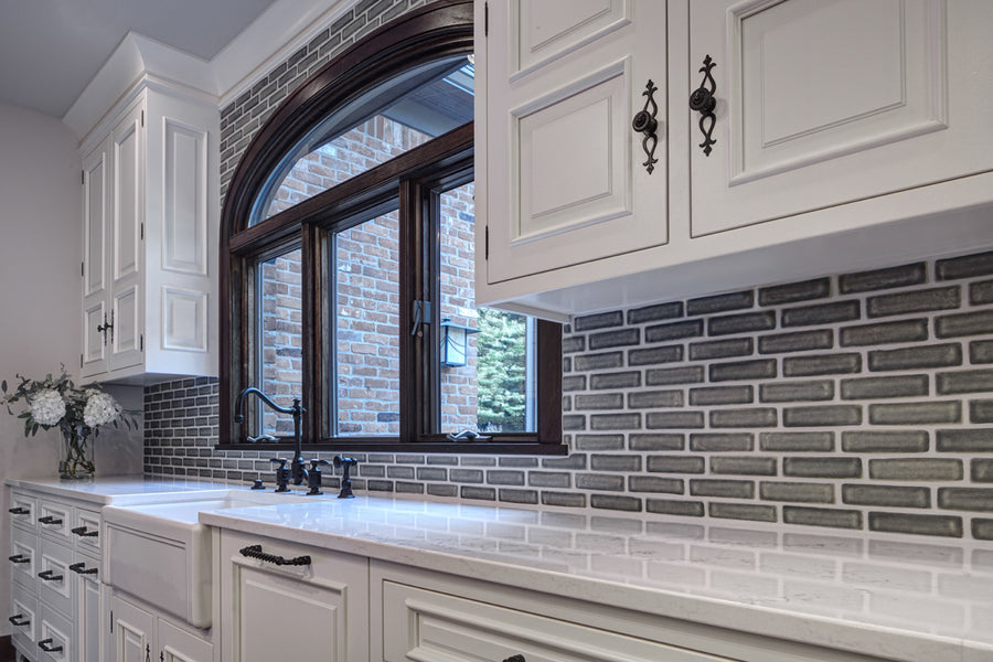White quartz countertops with ornate white cabinets showcase the pale gray of the subway tiles. 