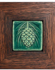 The ceramic Pinecone Tile has a high relief design with one large pinecone in the center and long spindly pine needles framing it. This tile is in the matte blueish-green Pewabic Green glaze which beautifully offsets the deep reddish brown hue of the oak frame.