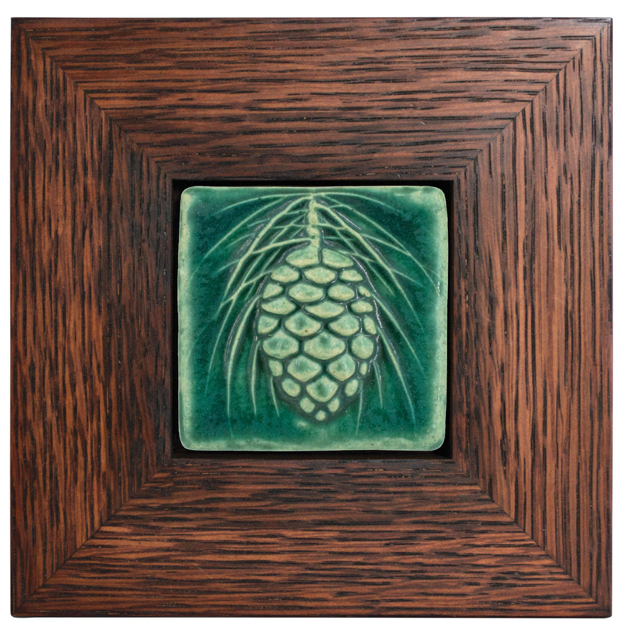 The ceramic Pinecone Tile has a high relief design with one large pinecone in the center and long spindly pine needles framing it. This tile is in the matte blueish-green Pewabic Green glaze which beautifully offsets the deep reddish brown hue of the oak frame.
