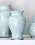 Three vases in various shapes sit on a white shelf- they all feature the glossy pale blue-gray Frost glaze. A close-up of the Frost glaze shows crazing on its surface- this gives the appearance of tiny cracks on the glaze's surface.