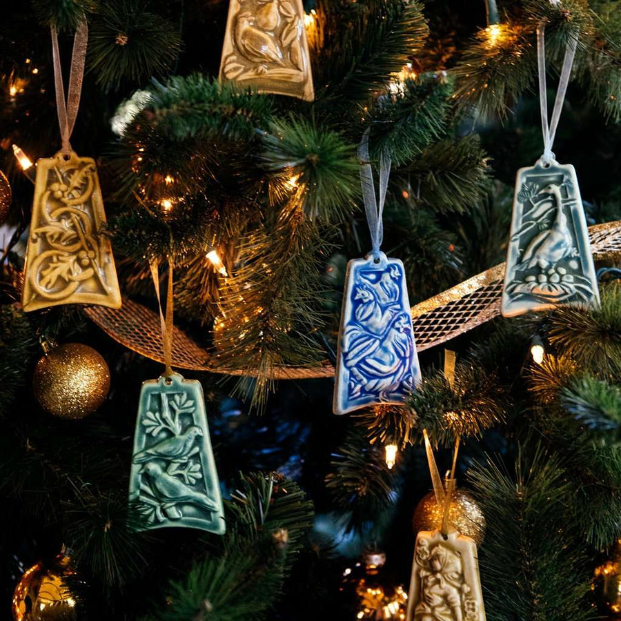 Various bell-shaped ceramic ornaments are hung on a lit Christmas tree.
