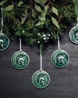 Five Spartan ornaments are hung against a wall from a thick cropping of seasonal green foliage.