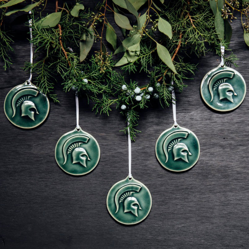 Five Spartan ornaments are hung against a wall from a thick cropping of seasonal green foliage.