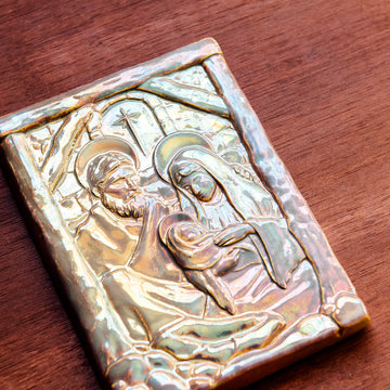 The Nativity Tile features the haloed holy family - Joseph, Mary and Baby Jesus - embracing under the wooden beams of the stable. Behind them, a window in the stone wall gives a glimpse of the Bethlehem star. This tile features the pinkish gold metallic Blush Iridescent finish which has many variations. Depending on the lighting in the room, these pieces will pick up different hues.