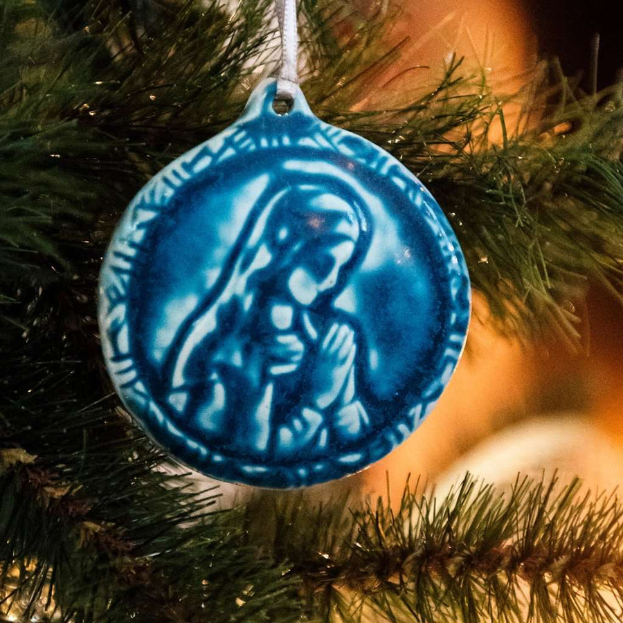 This ceramic Blessed Virgin Mary Ornament depicts Mary with head bowed and hands together in prayer. It is glazed in a matte blue Peacock glaze.