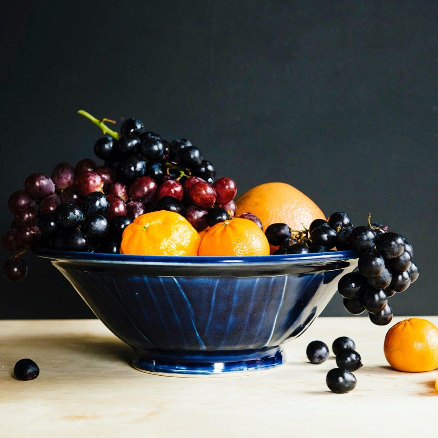 The Harvest Bowl is a large serving bowl with wide, sloped sides and a small round base. The wide sides have a slipped texture that ends in a thick lip at the top. This Harvest Bowl features the glossy deep dark blue Midnight glaze with a creamy white interior.
