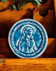 This ceramic Blessed Virgin Mary tile depicts Mary with head bowed and hands pressed together in prayer. It is glazed in a matte blue Peacock glaze.