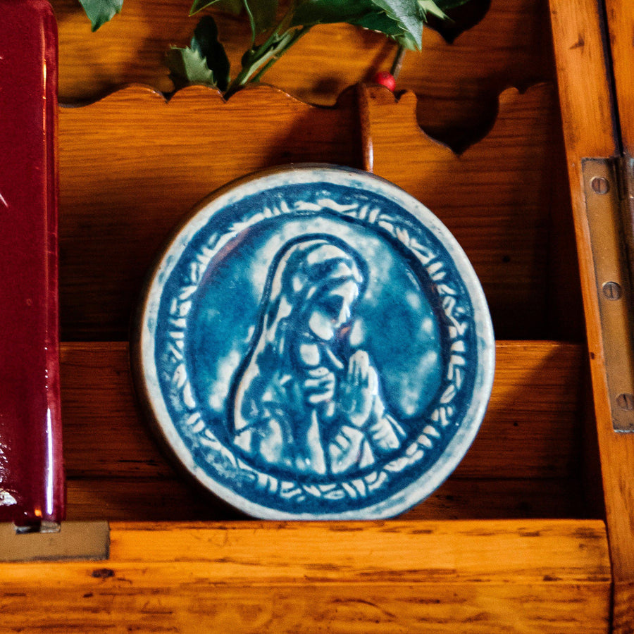 This ceramic Blessed Virgin Mary tile depicts Mary with head bowed and hands pressed together in prayer. It is glazed in a matte blue Peacock glaze.