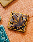 The molasses glazed maple leaf tile is featured. This tile is a deep glossy brown.