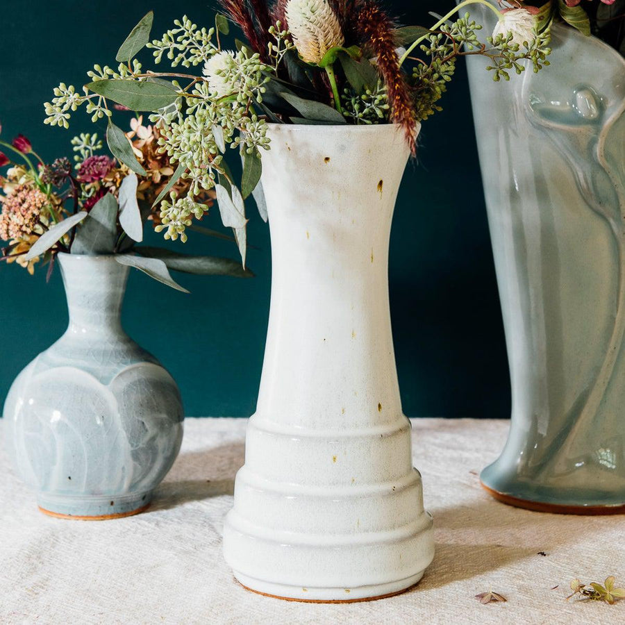 A Birch Step Vase sits among glossy pale blue Frost glazed pieces. They compliment each other well.