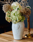 A Birch Pinecone vase holds a large bouquet of bushy hydrangeas. 