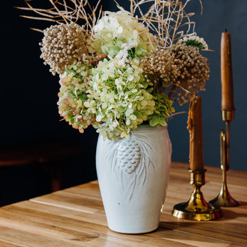 A Birch Pinecone vase holds a large bouquet of bushy hydrangeas. 
