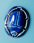 A Lapis scarab paperweight sits on a smooth pale blue background.