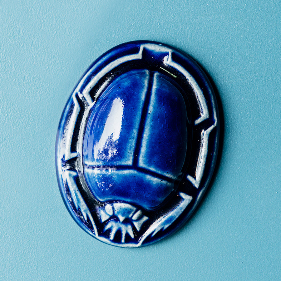 A Lapis scarab paperweight sits on a smooth pale blue background.