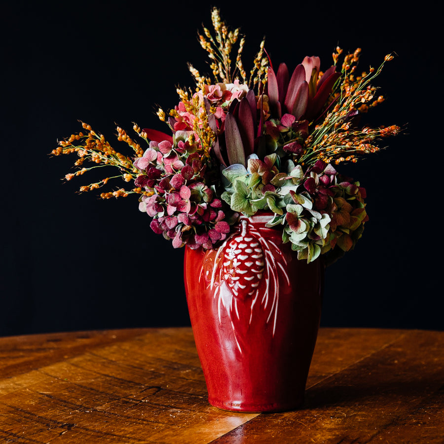 This Pinecone vase features the the glossy, deep red Winterberry glaze. The glaze breaks at the raised Pinecone detail on the vase, letting the ivory clay poke through and highlighting the intricate design.