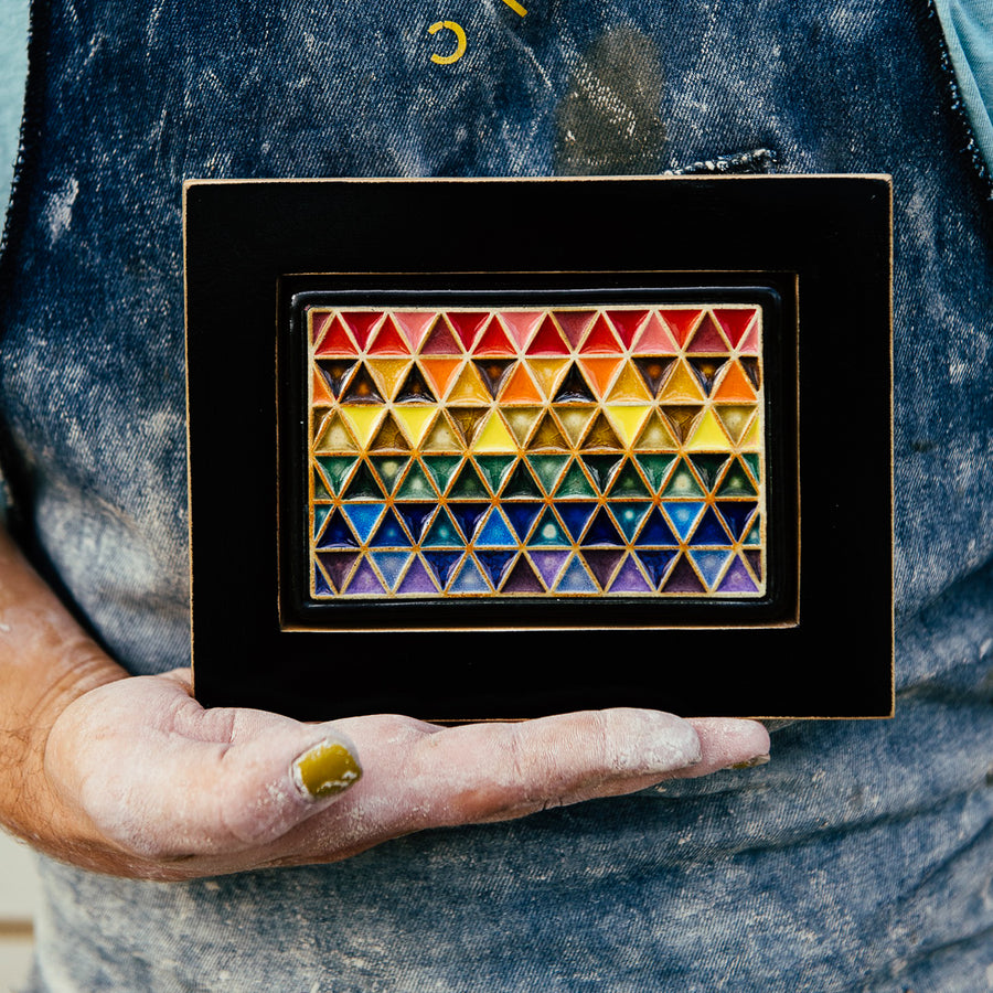 A Pewabic Artisan holds the framed Pride Tile in their dusty hands against their well-worn apron.