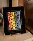 The 4x6 Pride Tile features lines of interlocking triangles, the colors on the triangles start at red and end in indigo- creating the rainbow Pride flag. The bright pattern is contained in a black border. The frame is a black painted reclaimed wood- giving a smooth appearance.