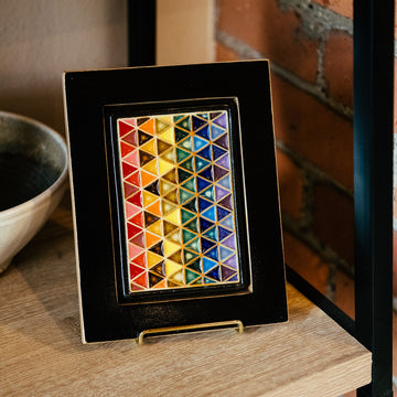 The 4x6 Pride Tile features lines of interlocking triangles, the colors on the triangles start at red and end in indigo- creating the rainbow Pride flag. The bright pattern is contained in a black border. The frame is a black painted reclaimed wood- giving a smooth appearance.