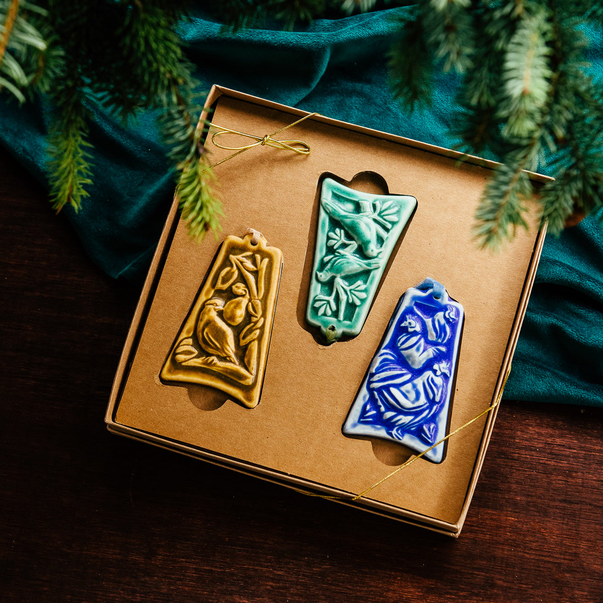 Three ceramic ornaments are sitting in a gift box and placed under a Christmas tree.