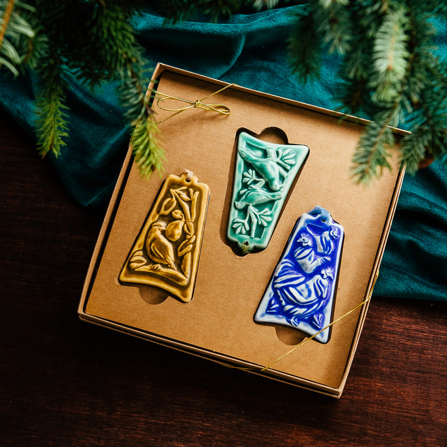 Three ceramic ornaments are sitting in a gift box and placed under a Christmas tree.