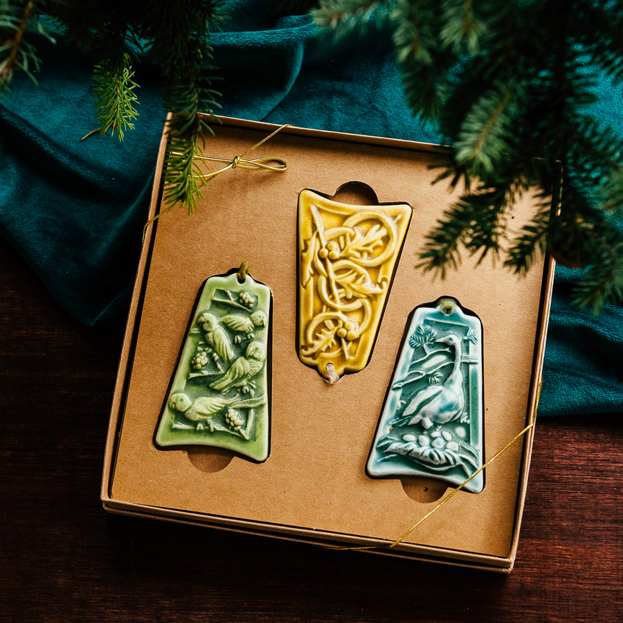 Three ceramic ornaments are sitting in a gift box and placed under a Christmas tree.