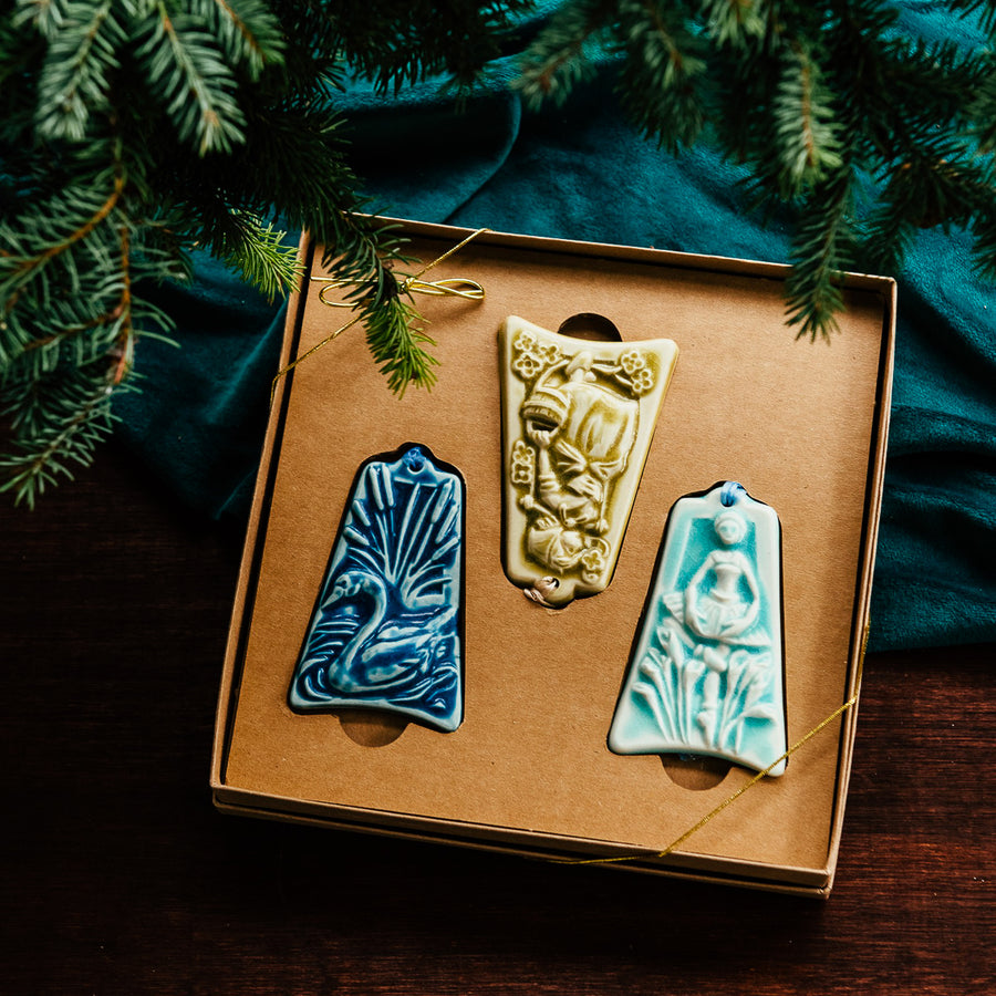 Three ceramic ornaments are sitting in a gift box and placed under a Christmas tree.