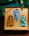Three ceramic ornaments are sitting in a gift box and placed under a Christmas tree.