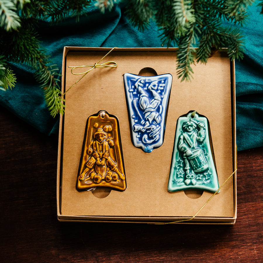 Three ceramic ornaments are sitting in a gift box and placed under a Christmas tree.