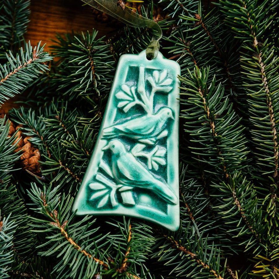 The bell-shaped Two Turtle Doves Ornament features two doves siting on the branches of a leafy tree.