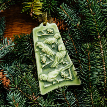 The bell-shaped Four Calling Birds Ornament features four parrots siting on the branches of a berry-covered tree. The ornament is glazed in a matte green color.
